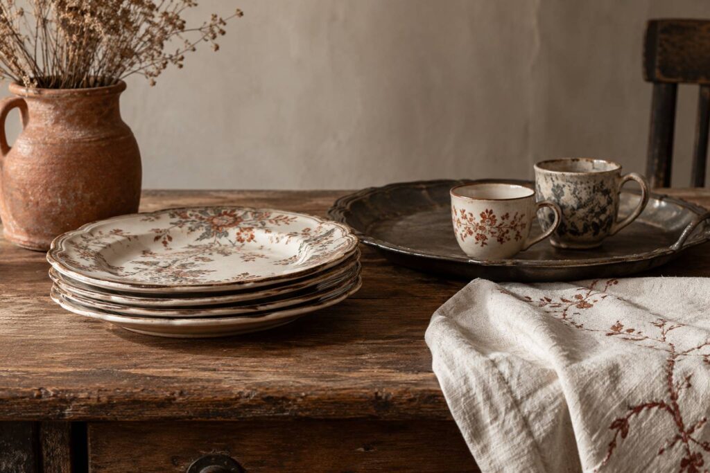 Pile d’assiettes anciennes à décor floral posée sur une table en bois patiné