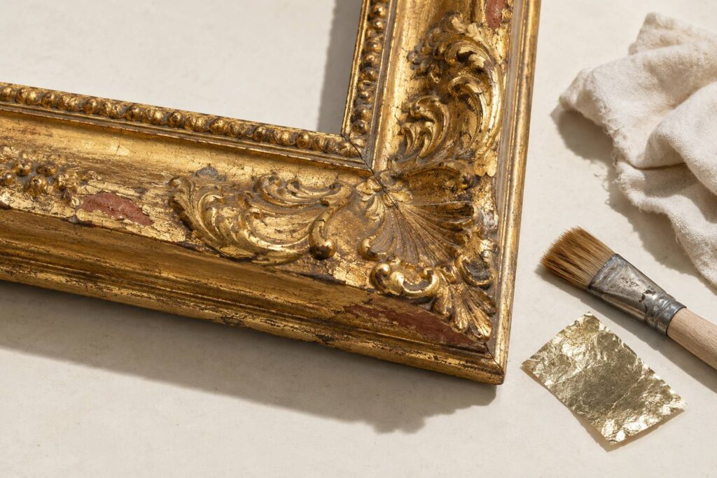 Coin de cadre ancien doré sur fond neutre, relief de feuille d'or révélé par une lumière frontale